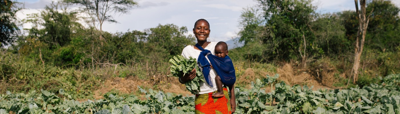 Vrouw met baby in Uganda houdt groenten vast