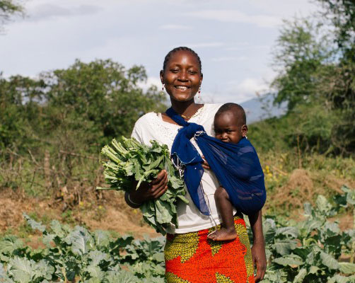 Vrouw met baby in Uganda houdt groenten vast